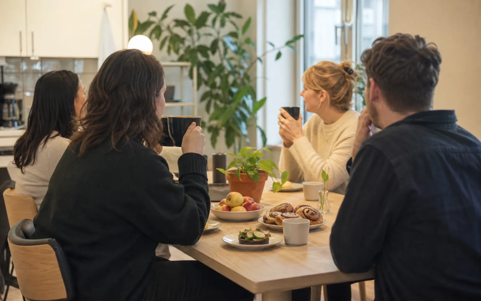 Fyra kollegor sitter runt ett bord med kaffe, kanelbullar och frukt