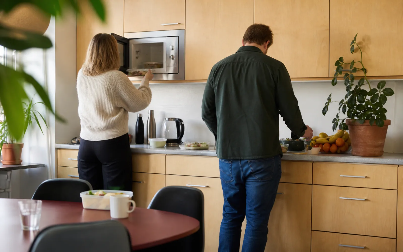 Ett kontorspentry med mikrovågsugn, fruktskål och kollegor som gör i ordning lunch