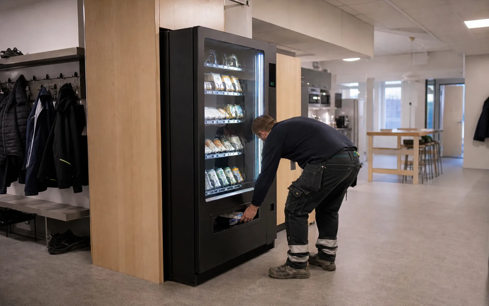 En person i arbetskläder hämtar något ur en varuautomat i ett omklädningsrum