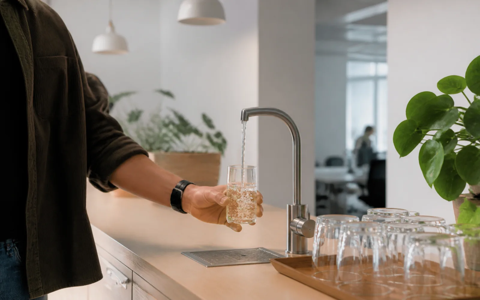 Ett glas fylls med kolsyrat vatten ur en fast kran i ett kontorskök